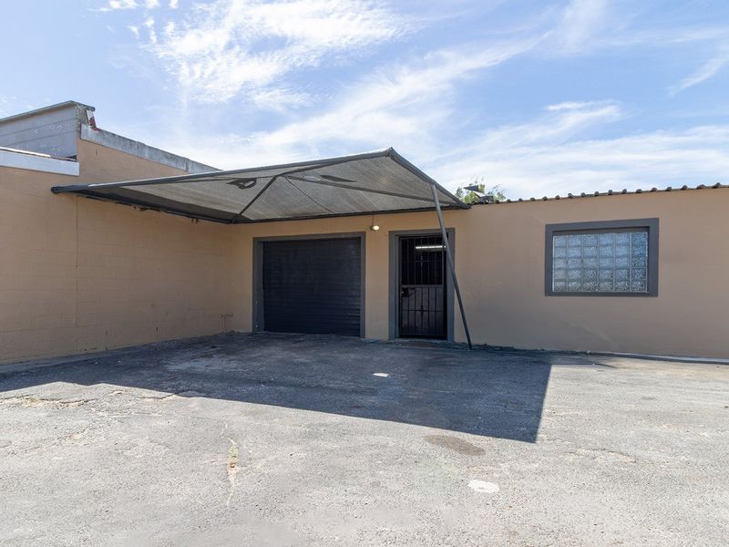 Exterior view of a property featuring a garage, security gate, shade sail, and a glass block window, with an asphalt driveway.
