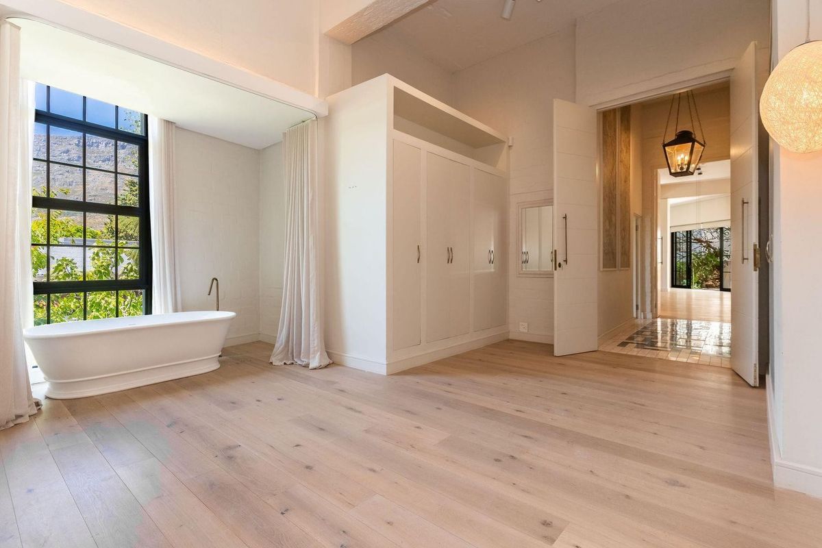 Spacious bedroom featuring light oak flooring, built-in cabinetry, and a freestanding bathtub positioned by a large window with mountain views.