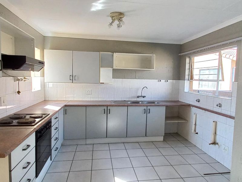A dated kitchen featuring built-in cabinetry, laminate countertops, an electric hob, and an oven, with tiled flooring and splashbacks throughout.