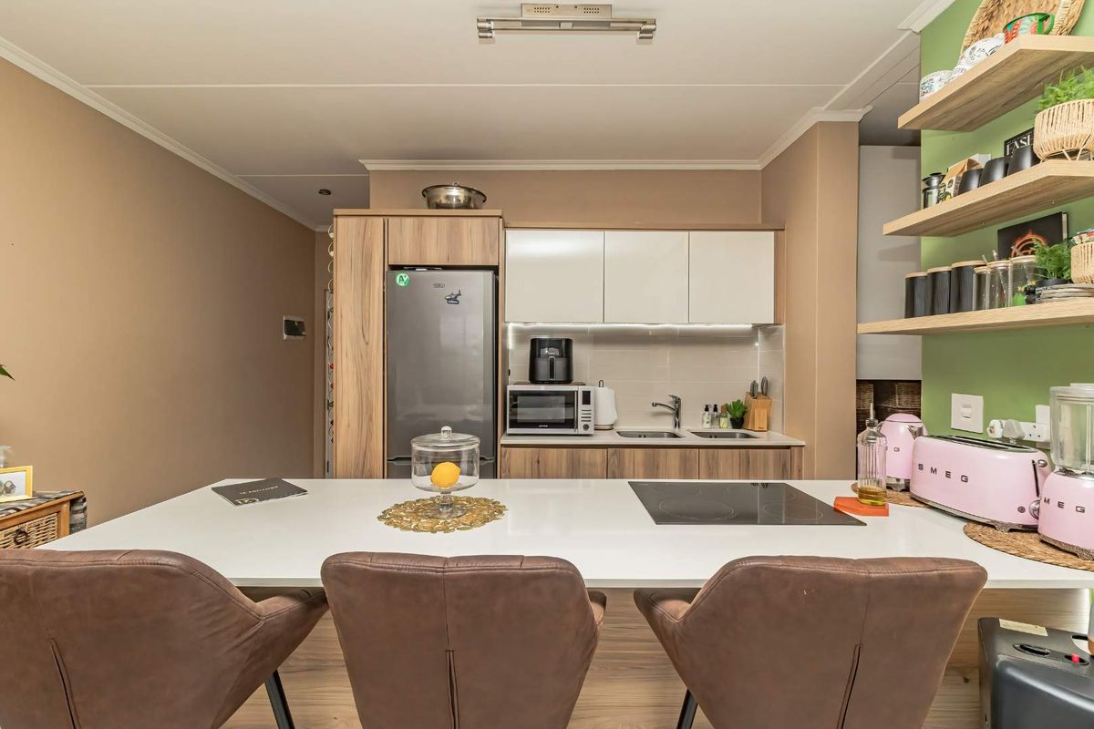 Modern kitchen featuring wood-tone cabinetry, a white breakfast bar with an integrated electric cooktop, and open shelving against a green accent wall.
