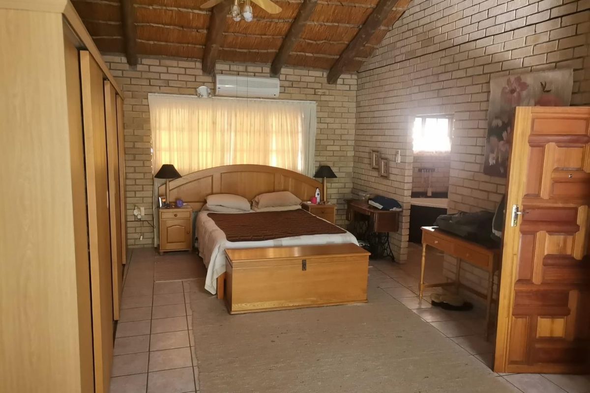 Spacious bedroom featuring exposed brick walls, a high vaulted ceiling with exposed timber beams, tiled flooring, and a built-in wardrobe.