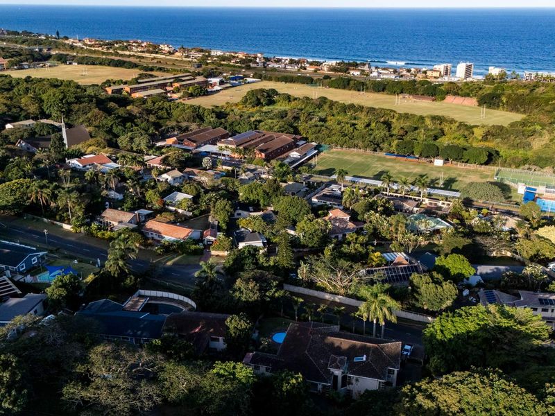 An aerial view of a coastal residential neighborhood, showcasing the property's proximity to the ocean, local sports fields, and surrounding greenery.