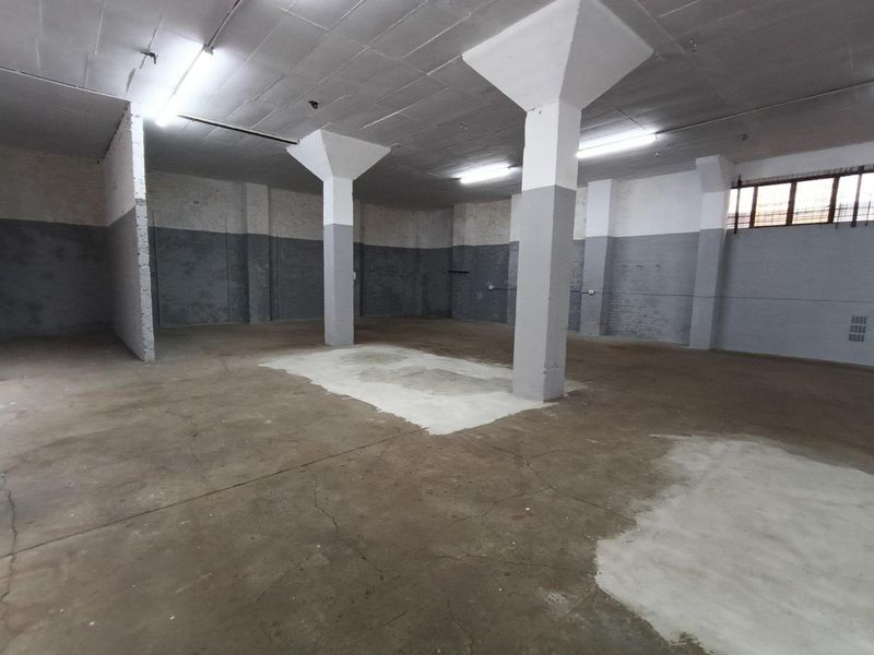 Spacious industrial utility area featuring concrete flooring, structural columns, and overhead fluorescent lighting, suitable for storage or workshop use.