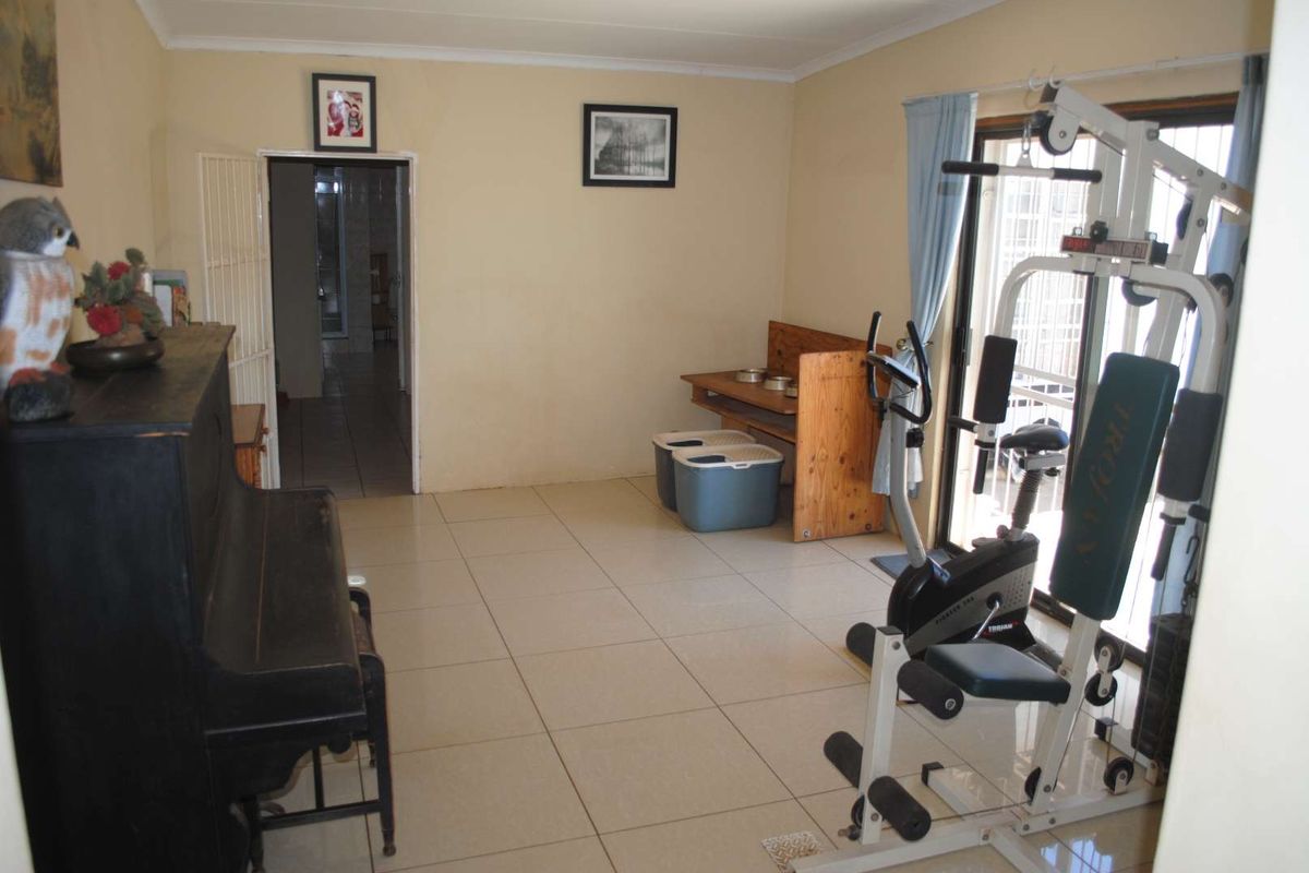 A multi-purpose living area featuring tiled flooring and sliding glass doors leading to an outdoor space, currently utilized as a home gym.