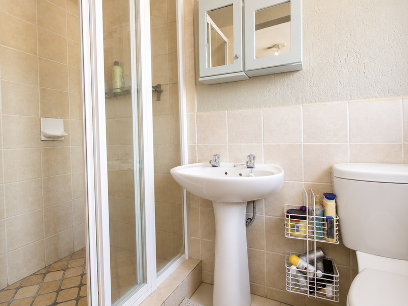 A functional bathroom featuring a pedestal basin, a shower enclosure with tiled walls, and a standard toilet.