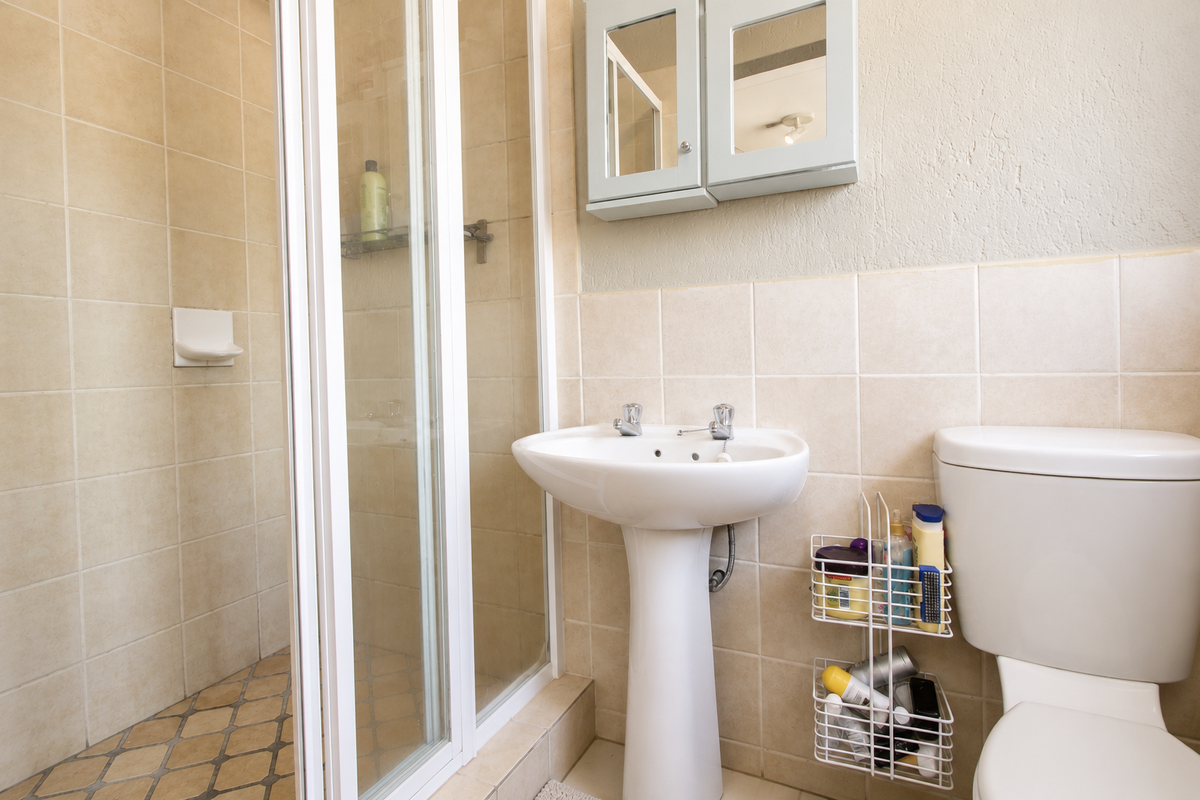 A functional bathroom featuring a pedestal basin, a shower enclosure with tiled walls, and a standard toilet.