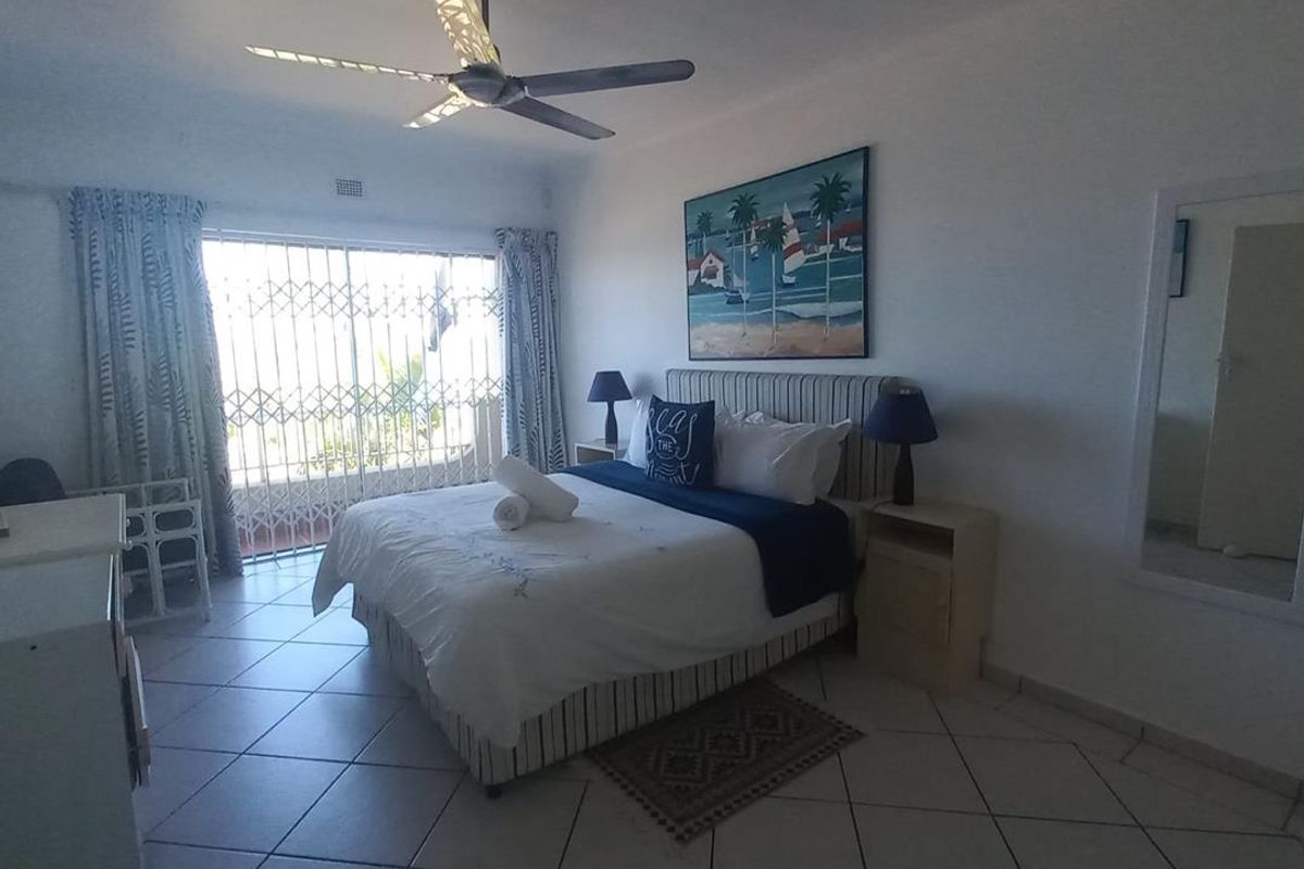 Spacious bedroom featuring tiled flooring, a ceiling fan, and sliding glass doors with security gates leading to an outdoor area.