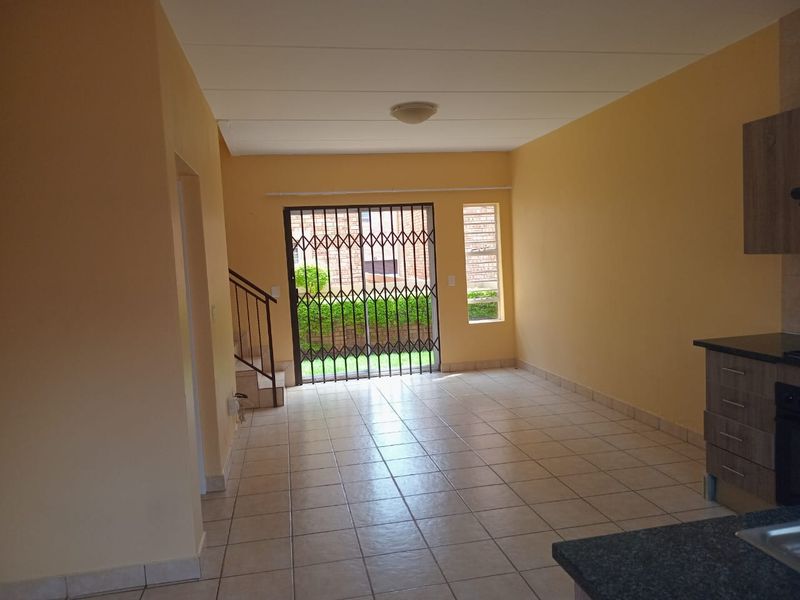 Spacious open-plan living area featuring tiled floors, a staircase with metal railing, and a functional kitchen with built-in cabinetry and granite countertops.