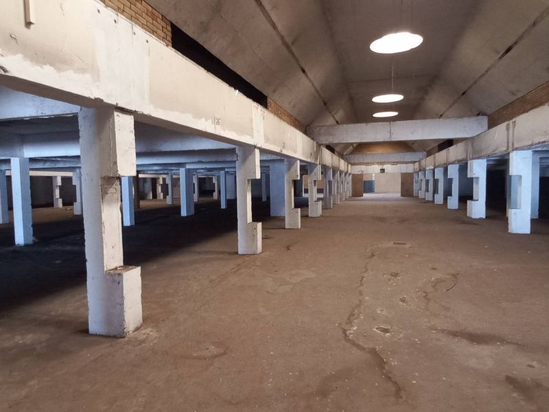 Expansive industrial warehouse space featuring high vaulted ceilings, exposed concrete structural columns, and durable concrete flooring throughout.