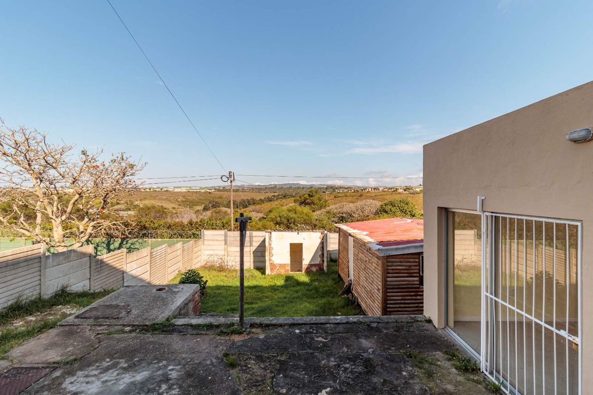 Rear exterior view featuring a concrete patio, sliding door with security gate, and a large backyard with a secondary outbuilding and boundary wall.