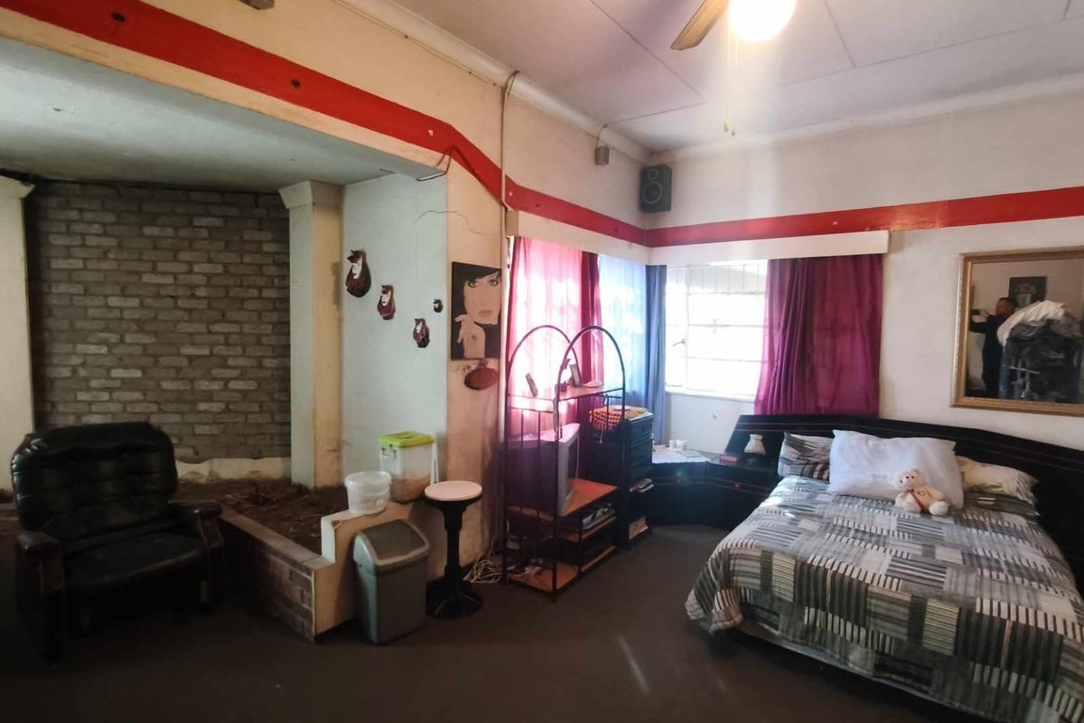 A bedroom featuring exposed brickwork, a ceiling fan, and a built-in headboard structure, requiring cosmetic updates to improve the overall finish.