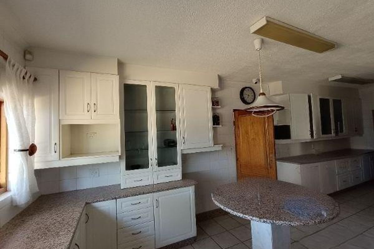 Spacious kitchen featuring white cabinetry, granite countertops, a central breakfast bar, and tiled flooring, offering a functional layout with ample storage space.