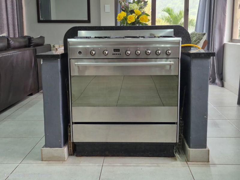A kitchen area featuring a stainless steel freestanding gas stove set within a granite-topped island with tiled flooring.