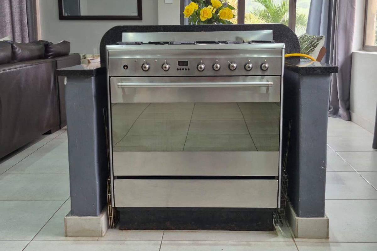 A kitchen area featuring a stainless steel freestanding gas stove set within a granite-topped island with tiled flooring.
