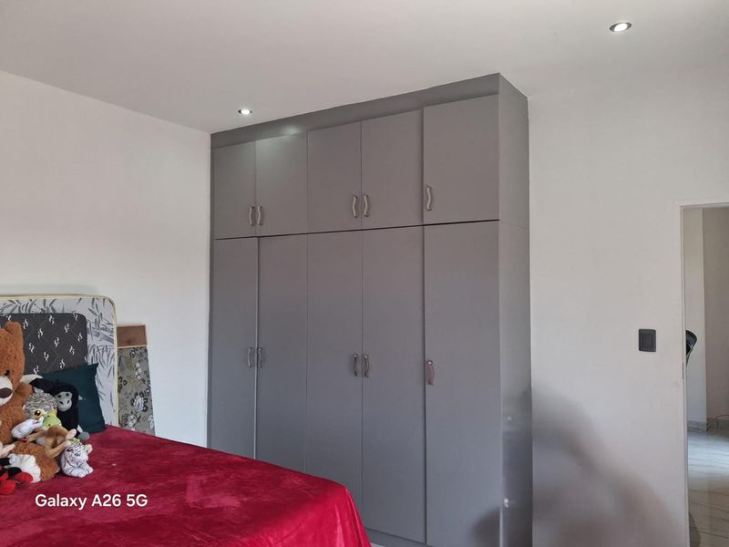 A bedroom featuring modern grey built-in cupboards with ample storage and recessed ceiling downlights.