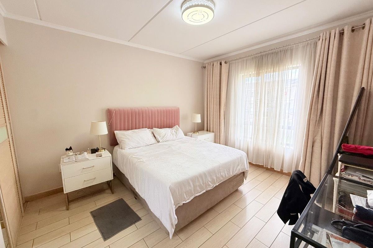 A well-lit bedroom featuring light-toned tiled flooring, a built-in wardrobe, and large windows with curtains, creating a comfortable and functional living space.