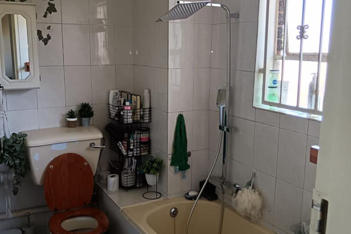 A functional bathroom featuring a built-in bathtub with a modern shower head, a toilet, and tiled walls with a window for natural light.