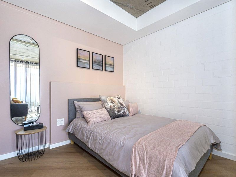 A modern bedroom featuring a painted brick feature wall, exposed concrete ceiling detail, and warm laminate flooring.