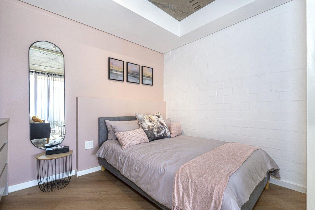 A modern bedroom featuring a painted brick feature wall, exposed concrete ceiling detail, and warm laminate flooring.
