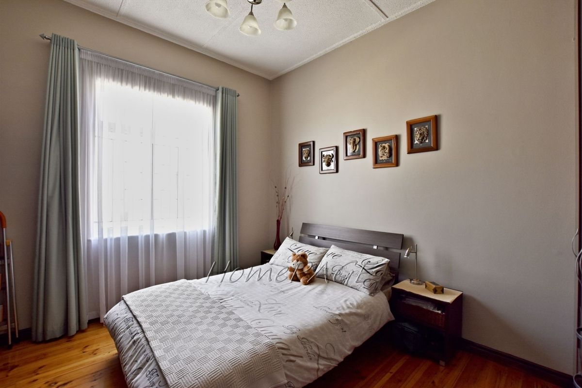 A well-lit bedroom featuring polished timber flooring and a large window with curtain tracks.