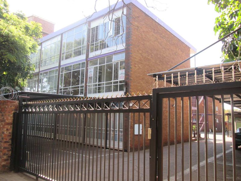 Exterior view of a multi-story apartment building featuring a brick facade, large windows, and a secure gated entrance with a paved driveway.