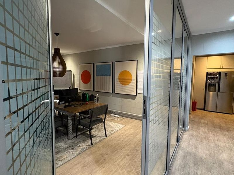 Modern office space featuring glass partition walls, laminate flooring, and recessed lighting, creating a bright and professional work environment.