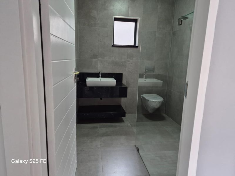 Modern bathroom featuring a wall-mounted vanity with a vessel sink, wall-hung toilet, and a glass-enclosed shower with contemporary grey tiling.
