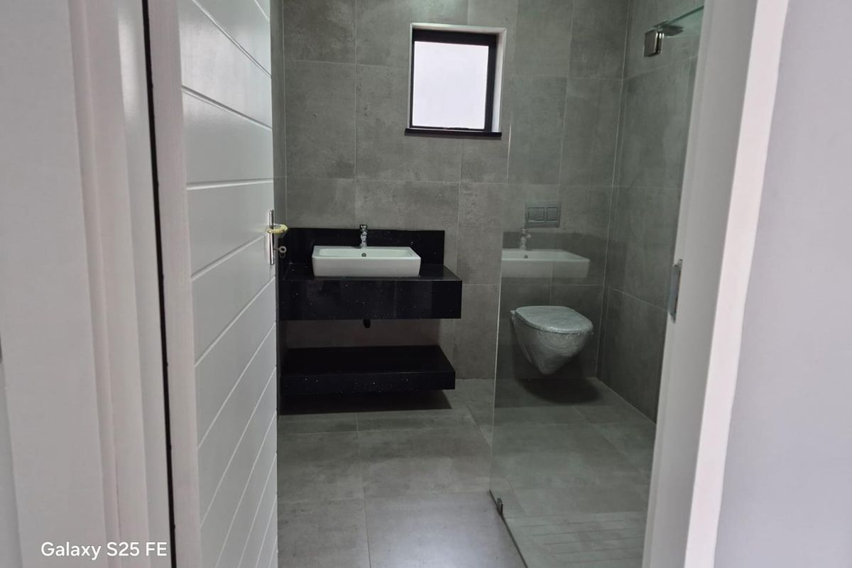 Modern bathroom featuring a wall-mounted vanity with a vessel sink, wall-hung toilet, and a glass-enclosed shower with contemporary grey tiling.