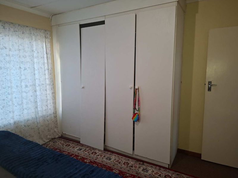 A bedroom featuring a built-in wardrobe with white doors, showing signs of wear and misalignment.
