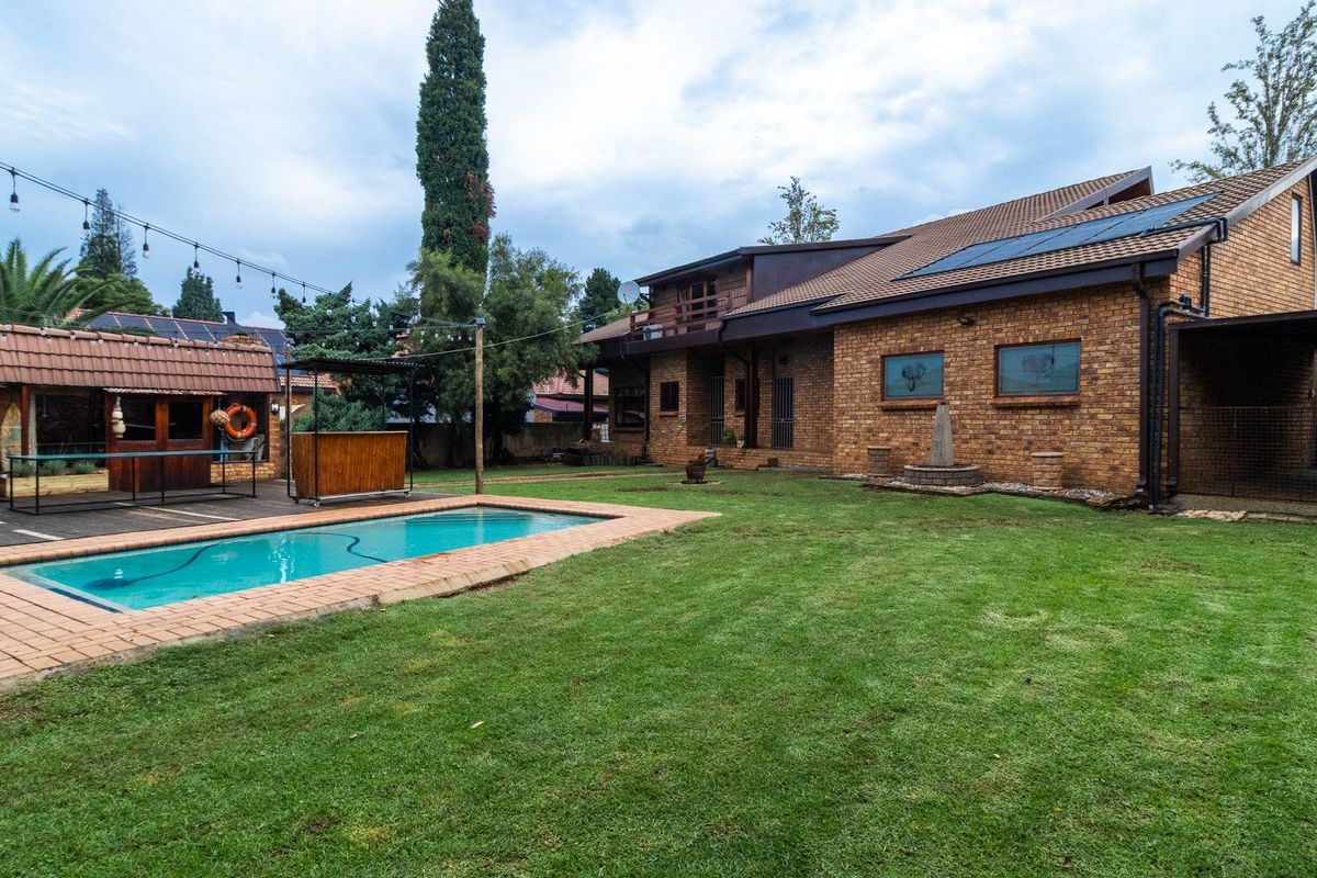 Spacious rear garden featuring a swimming pool, paved surround, and a covered outdoor entertainment area with brick facade architecture.