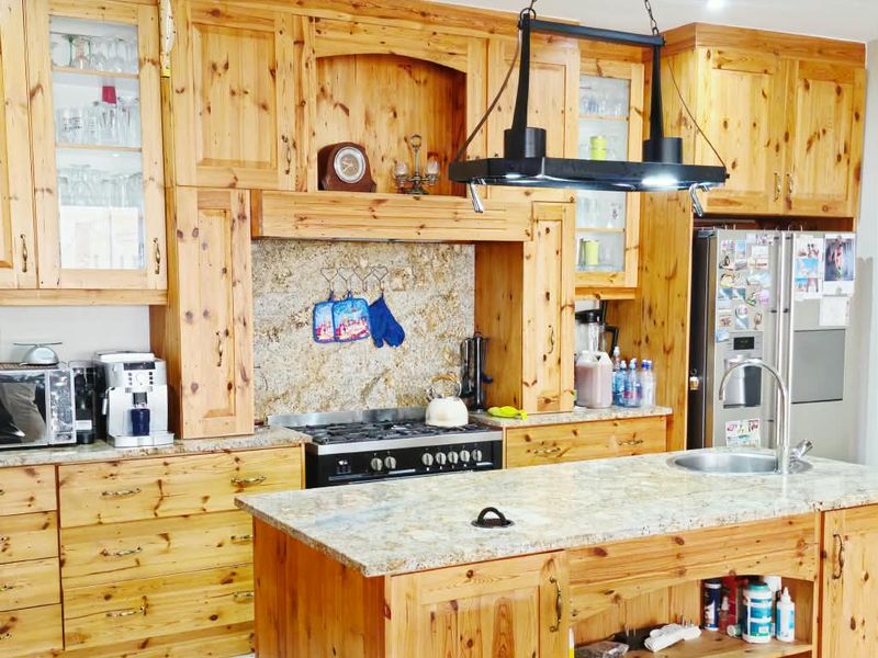 A spacious kitchen featuring extensive knotty pine cabinetry, granite countertops, a central island with a sink, and a built-in gas hob with an extractor fan.