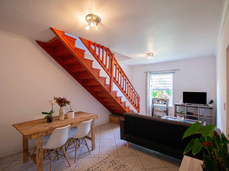 Open plan living and dining area featuring a prominent wooden staircase, tiled flooring, and natural light from the window.