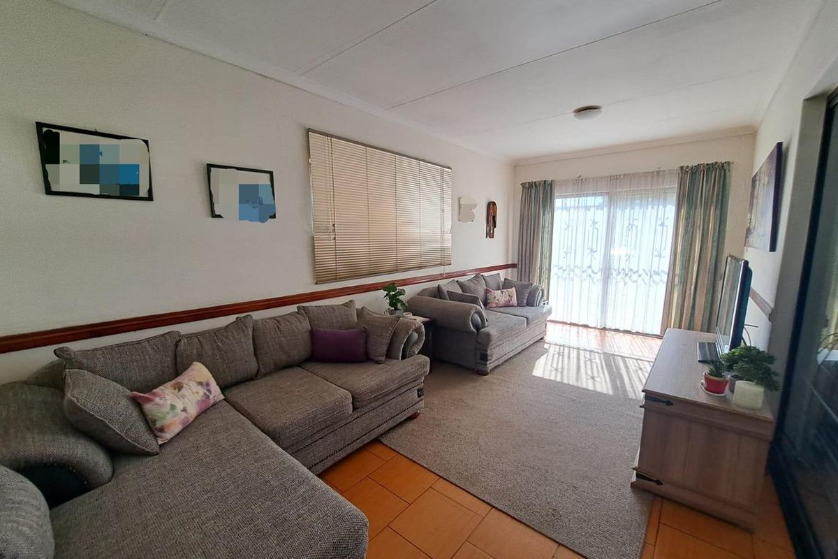 A spacious living room featuring tiled flooring, a large window with fitted blinds, and sliding glass doors providing access to the exterior.
