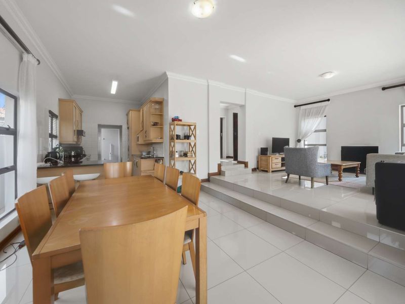 Spacious open-plan living and dining area featuring tiled floors, a sunken lounge, and a functional kitchen with built-in cabinetry and granite countertops.