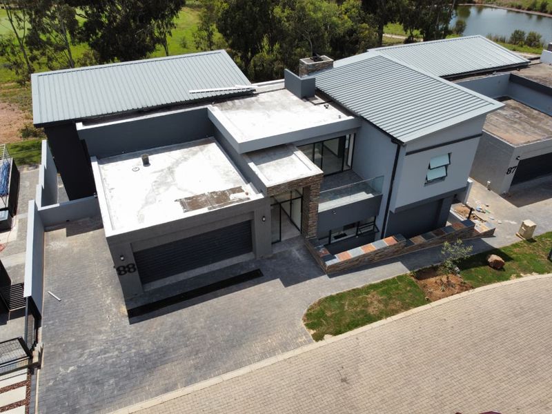 Aerial view of a modern cluster home featuring a metal roof, stone cladding accents, a paved driveway, and a double garage.