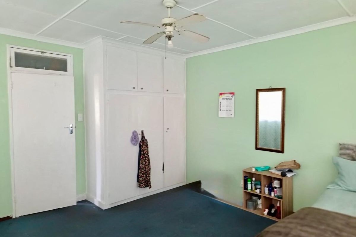 A bedroom featuring built-in cupboards, a ceiling fan, and carpeted flooring. The space offers a functional layout with potential for cosmetic updates.