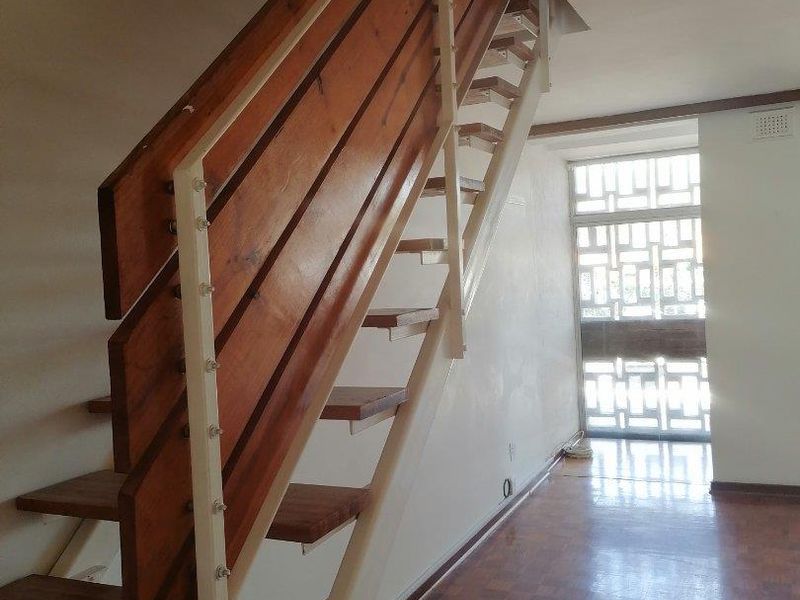 A bright hallway featuring a timber staircase, parquet flooring, and a decorative security screen, presenting a functional space with potential for cosmetic updates.