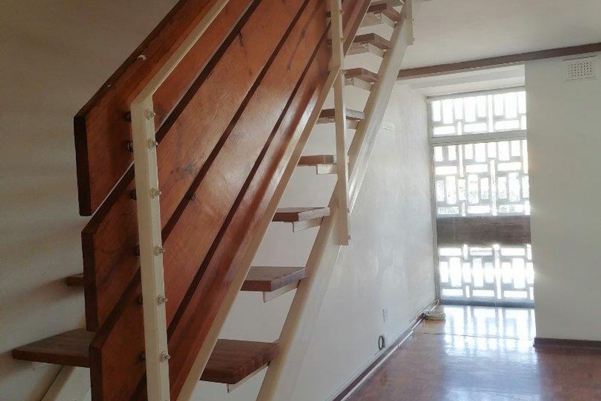 A bright hallway featuring a timber staircase, parquet flooring, and a decorative security screen, presenting a functional space with potential for cosmetic updates.