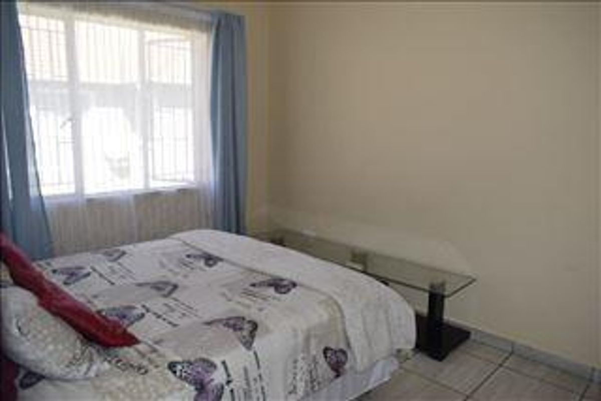 A bedroom featuring tiled flooring and a large window with security bars, providing natural light to the space.