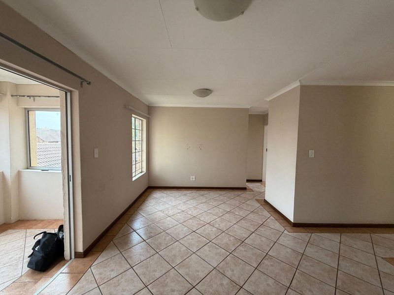 An empty, neutrally painted living area featuring tiled flooring, a sliding door leading to a balcony, and natural light from a side window.