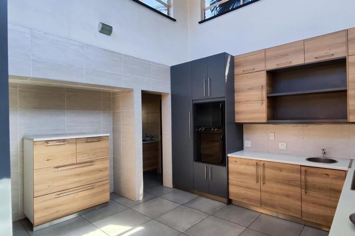 Modern kitchen featuring wood-grain cabinetry, dark grey integrated oven housing, tiled flooring, and a secondary scullery area visible through the doorway.
