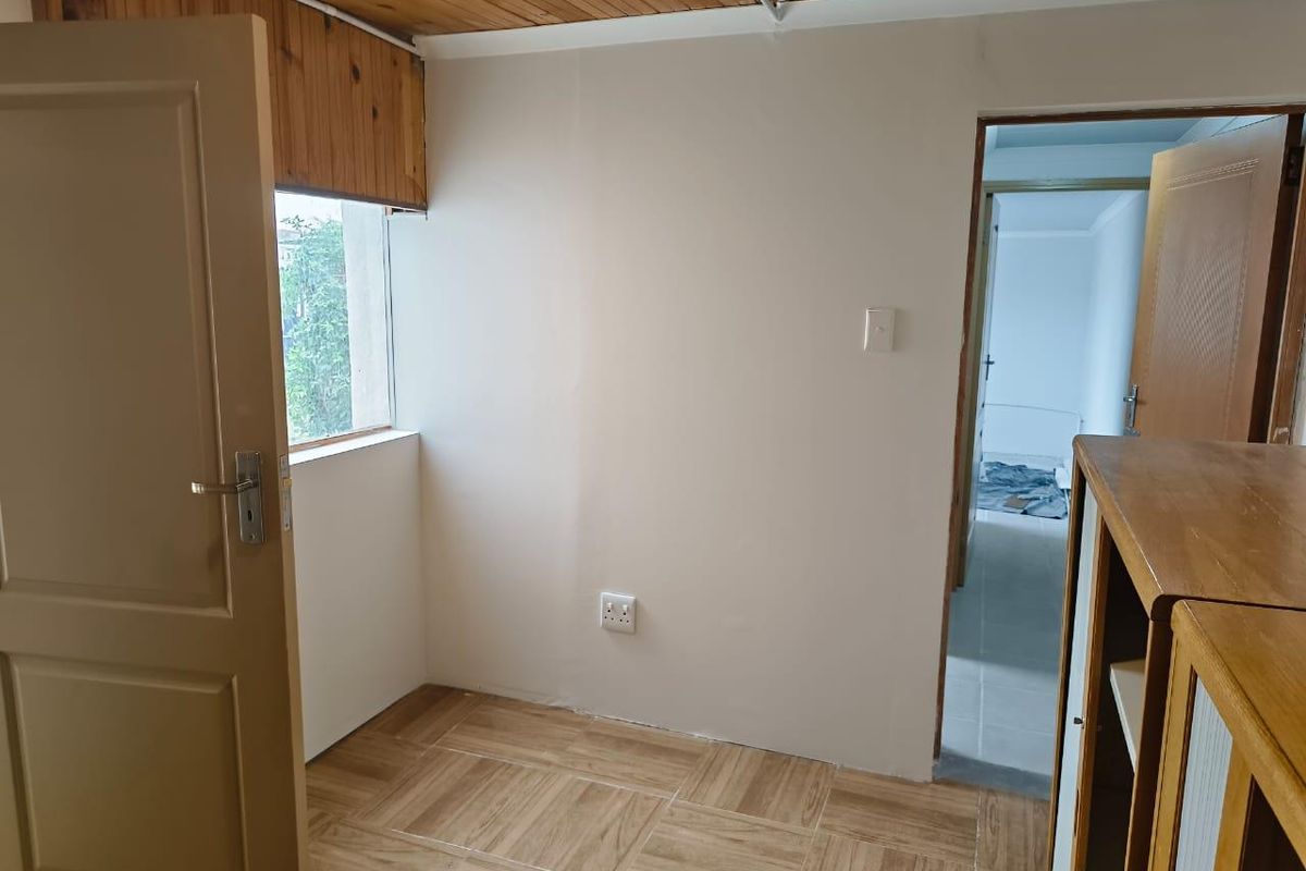 A small bedroom or study area featuring wood-paneled ceilings, tiled flooring, and a window overlooking the exterior.