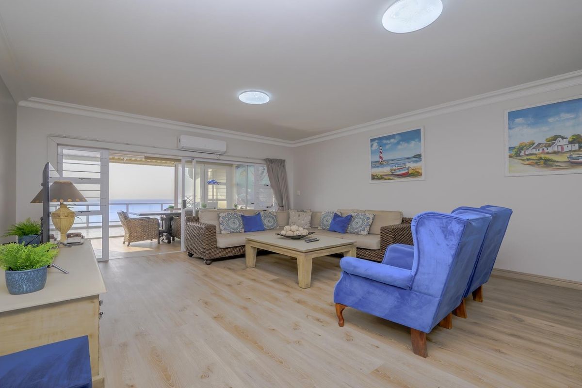 Spacious living room featuring light laminate flooring, cove molding, and large sliding glass doors that open onto a balcony with ocean views.
