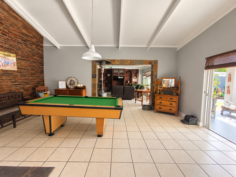 Spacious living area featuring a vaulted ceiling with exposed beams, a striking brick feature wall, ceramic tile flooring, and a stone-accented archway leading through.