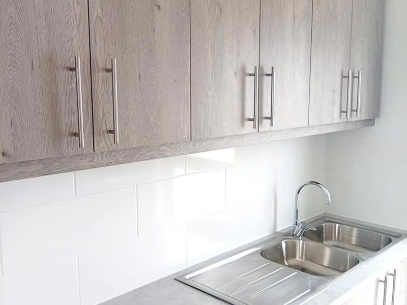 A clean, modern kitchen area featuring wood-grain cabinetry, a stainless steel double sink with chrome tap, and a white subway tile backsplash.