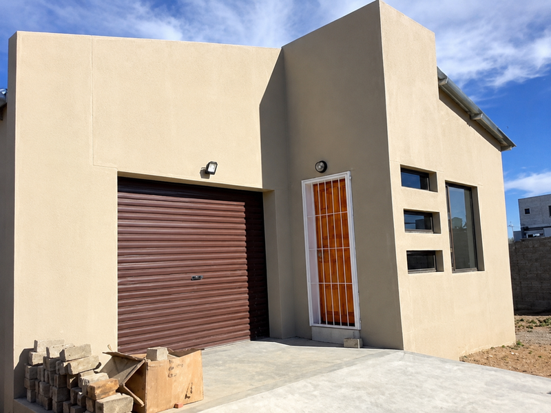 Modern single-story residential facade featuring a roller shutter garage door, secure entrance, and clean rendered exterior walls.
