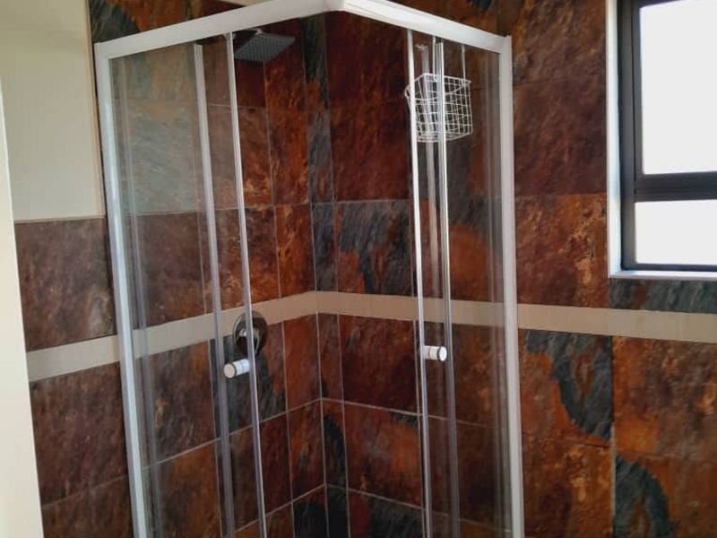 A bathroom featuring a corner shower enclosure with dark stone-look wall tiles and a window for natural light.