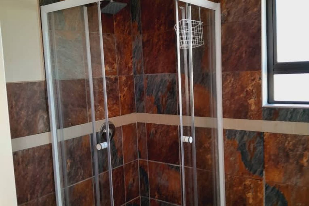 A bathroom featuring a corner shower enclosure with dark stone-look wall tiles and a window for natural light.