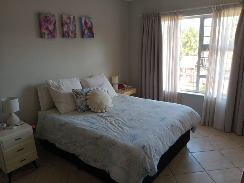 A well-lit bedroom featuring neutral wall tones, tiled flooring, and a large window with installed curtain tracks.