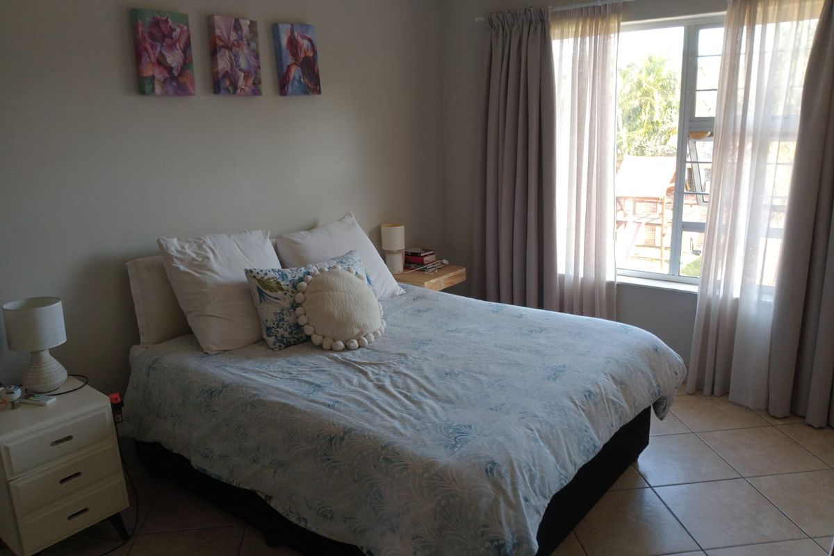 A well-lit bedroom featuring neutral wall tones, tiled flooring, and a large window with installed curtain tracks.
